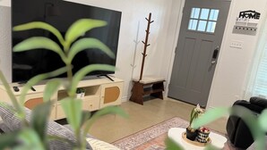 Una sala de estar con un televisor de pantalla plana grande, un perchero, una puerta gris y un letrero en la pared que dice 'HOME'.