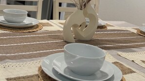 Una mesa de comedor con un florero de plantas secas, dos cuencos blancos y un mantel individual.