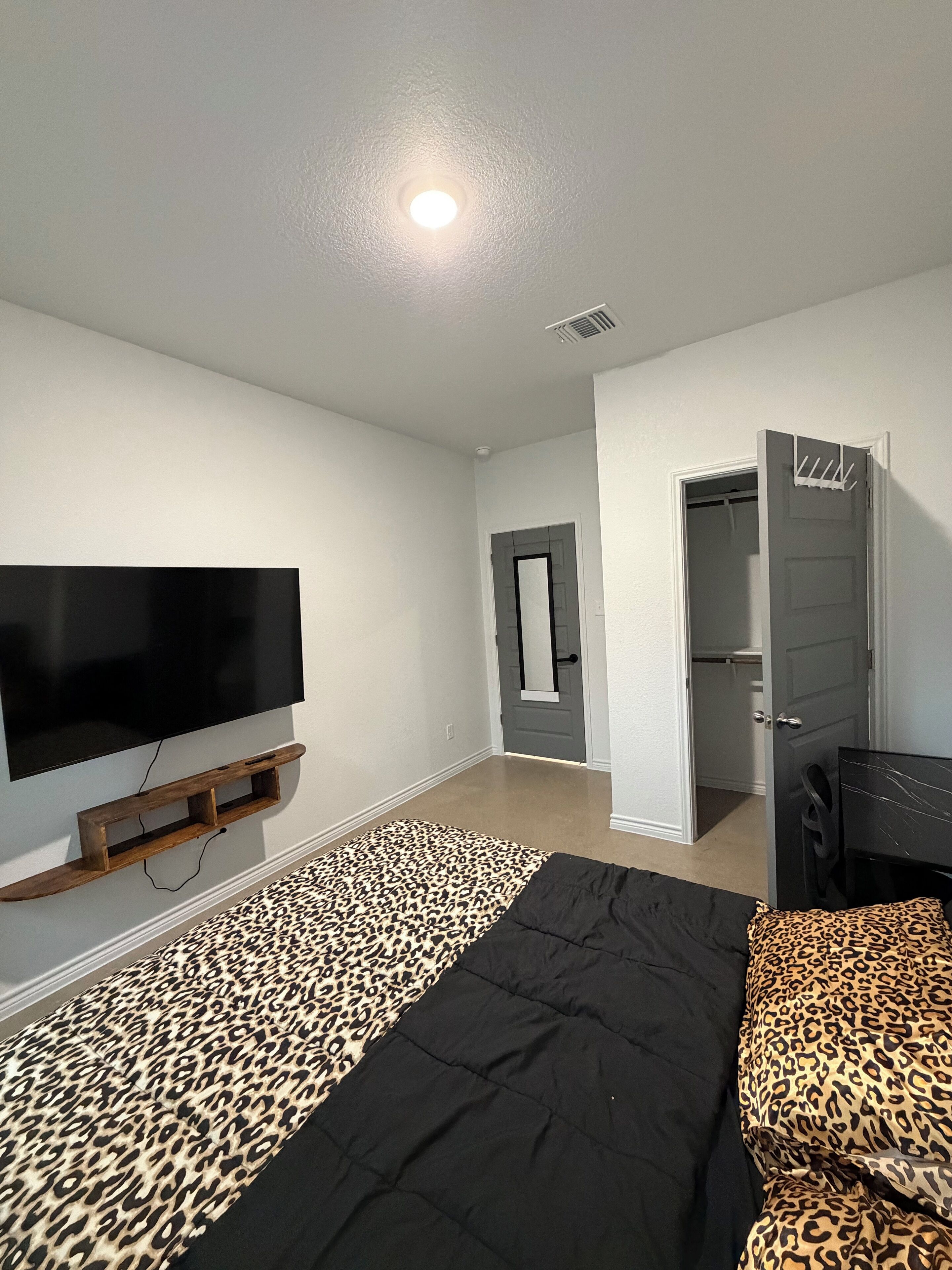 A bedroom with a bed, a television mounted on the wall, a closet, and a door leading to another room.