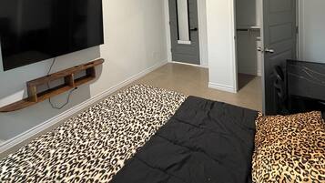 A bedroom with a bed, a television mounted on the wall, a closet, and a door leading to another room.