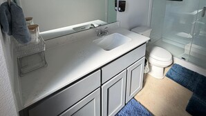 Un baño moderno con tocador blanco, cabina de ducha de vidrio y un inodoro.