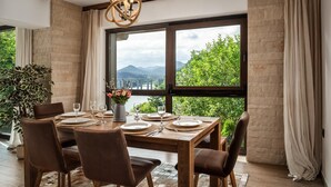 Comedor con una mesa grande dispuesta para seis personas, una planta en maceta y vistas a zonas verdes y montañas a través de amplios ventanales.