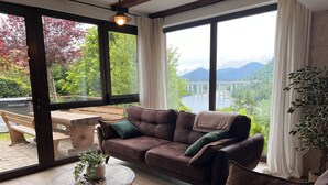 Una habitación acogedora con un sofá de cuero, una mesa redonda con una planta y vistas a un lago y montañas a través de amplios ventanales.
