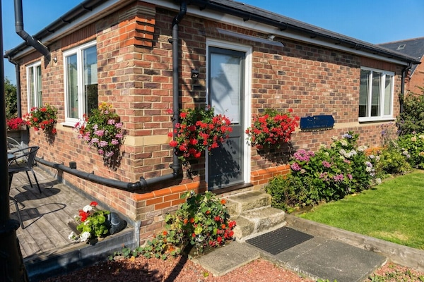 A sun-drenched brick cottage wrapped in vivid red geraniums welcomes you on arrival.