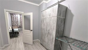 A room with a grey wardrobe, a drying rack, and a dining area with a table and chairs.