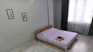 A bedroom with a bed, a patterned rug, and two framed artworks on the wall.