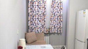 A small, modern kitchen with a dining table set for two, a refrigerator, and a patterned curtain.