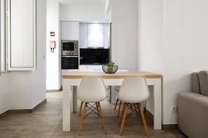 A modern kitchen with white cabinets, a wooden dining table, and two chairs. - Red Door Flat by Trip2Portugal (Figueira da Foz)