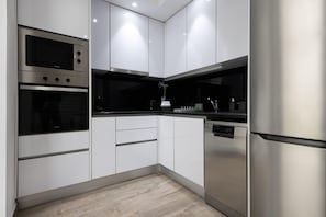 A modern kitchen with white cabinetry, stainless steel appliances, and a black countertop. - Red Door Flat by Trip2Portugal (Figueira da Foz)