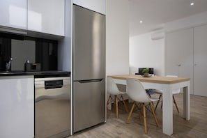 A modern kitchen with a built-in dishwasher, a stainless steel refrigerator, and a wooden dining table with white chairs. - Red Door Flat by Trip2Portugal (Figueira da Foz)