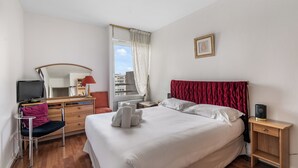 Ein Hotelzimmer mit Bett, Schreibtisch mit Computer, Stuhl, Fenster mit Vorhängen und Nachttisch.
