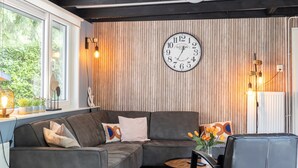 A modern living room with a sectional sofa, a round wooden coffee table, and a wall-mounted clock. - House & More Near the Ijsselmeer (Lemmer)