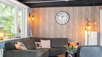 Una sala de estar moderna con un sofá modular, una mesa de centro redonda de madera y un reloj fijado a la pared.