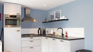 A modern kitchen with white cabinetry, a stainless steel range hood, a gas stove, and a black trash bin. - House & More Near the Ijsselmeer (Lemmer)