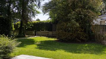 Un jardín bien cuidado con un sendero pavimentado, una valla de madera y abundante vegetación.