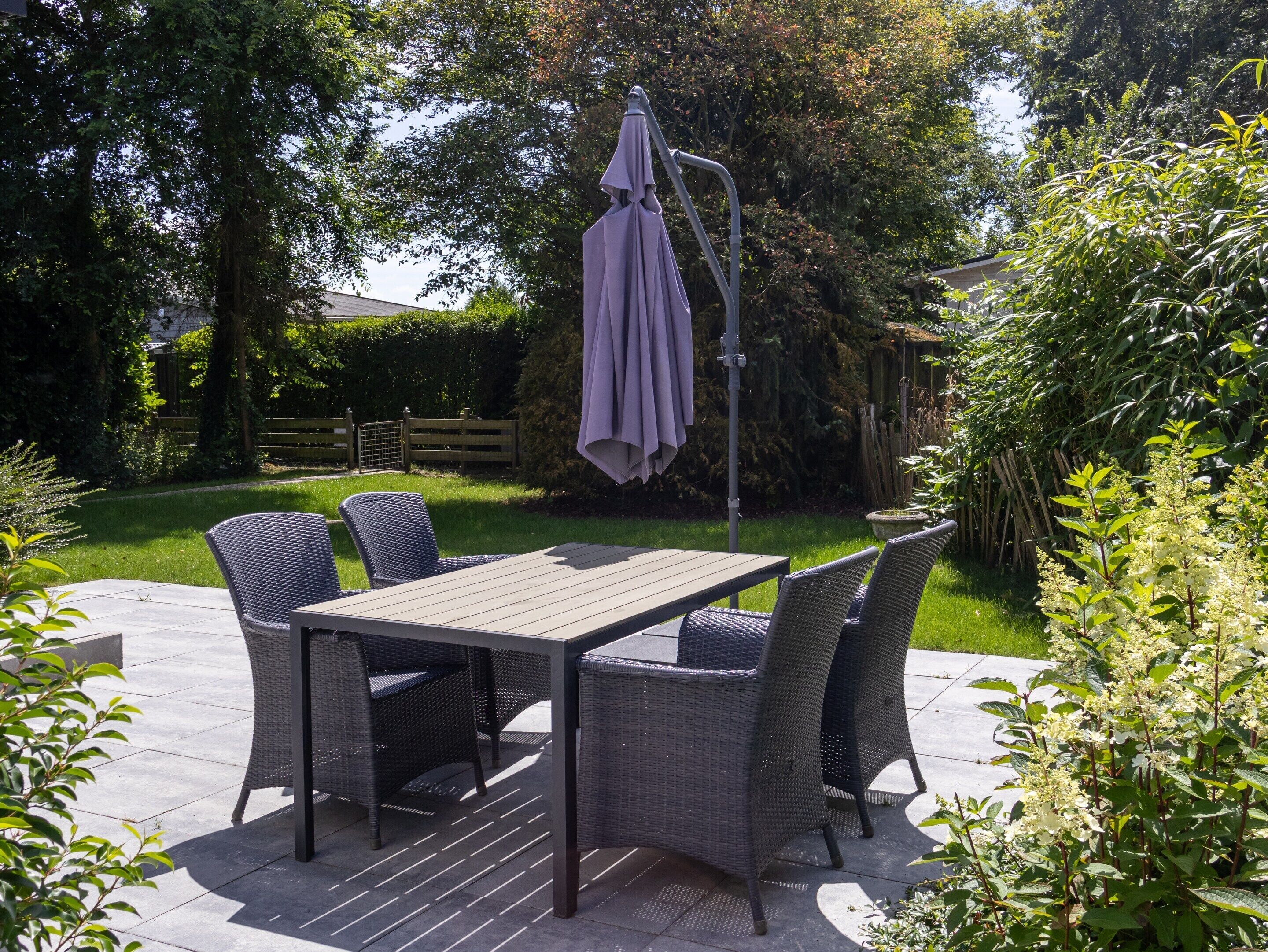 An outdoor patio with a table and chairs, surrounded by greenery and a wooden fence.