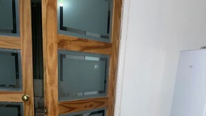 Ein Zimmer mit einer Holztür, verblassten Glasscheiben, einer weißen Wand und einem weißen Kühlschrank.