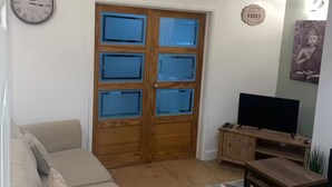 Ein Wohnzimmer mit einem beigefarbenen Sofa, einem Holztisch, einer TV-Konsole und einem gemusterten Teppich.