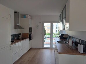 Eine moderne Küche mit weißen Schränken, einer Holzarbeitsplatte und Blick auf einen Parkplatz durch eine Glastür.
