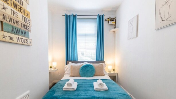 Ein Schlafzimmer mit einem Bett, blauen Vorhängen, einem an der Wand montierten Heizkörper und einem Nachttisch mit einer Lampe.