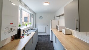 Eine kleine Küche mit weißen Schränken, einer Holzarbeitsplatte, einem eingebauten Backofen und einem Fenster mit Blumentöpfen.