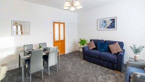Ein Zimmer mit Esstisch, Stühlen, einer Couch, einer Pflanze und einem Bild an der Wand.