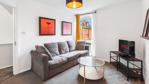 Una sala de estar moderna con un sofá gris, una mesa de centro redonda, un televisor sobre un mueble bajo y obras de arte enmarcadas en la pared.