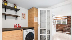 Cocina compacta con lavadora, repisas de madera, una puerta con paneles de vidrio esmerilado y vista a fachada de ladrillo.
