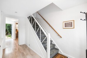 Una escalera con barandillas blancas y un pasamanos de madera, un letrero de bienvenida y una vista a una habitación con una puerta que da al exterior.