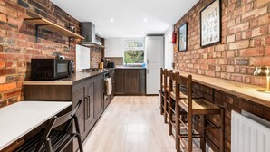 Una cocina con paredes de ladrillo, una mesa de madera y sillas, un microondas y un ventanal.