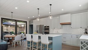 A modern kitchen with white cabinets, a blue island, and a dining area with a table and chairs. - Beautiful home located in OBP. Located on a beach block. Great home when visiting the island, all the amenities included. (OCEAN BEACH)