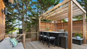 An outdoor deck with a wooden pergola, a barbecue grill, and a seating area with a sofa and chairs. - Beautiful home located in OBP. Located on a beach block. Great home when visiting the island, all the amenities included. (OCEAN BEACH)