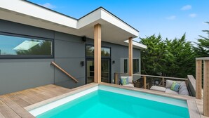 A modern house with a swimming pool, wooden deck, and a balcony with outdoor furniture. - Beautiful home located in OBP. Located on a beach block. Great home when visiting the island, all the amenities included. (OCEAN BEACH)