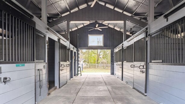 Un abri pour chevaux doté d’une toiture, de portes métalliques, d’un ventilateur de plafond et offrant une vue sur l’extérieur.