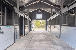 A covered stable with metal doors, a ceiling fan, and a view of the outside.