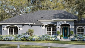Une maison à deux étages, avec une façade grise, un toit foncé et une porte d’entrée bleue.