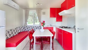 A modern kitchen with red cabinetry, a white countertop, and a dining area with a bench and chairs. - Mobile Home in Rabac With Shared Pool (Labin)