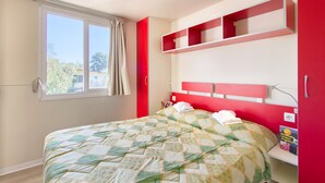 A bedroom with a bed, a window, a red wall, and a shelf with books. - Mobile Home in Rabac With Shared Pool (Labin)