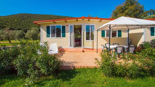 A single-story house with a patio, a covered outdoor seating area, and a view of a green hill. - Mobile Home in Rabac With Shared Pool (Labin)