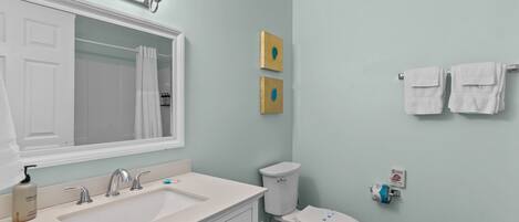 A bathroom with a white sink, two faucets, a mirror, a toilet, and two wall-mounted light fixtures.