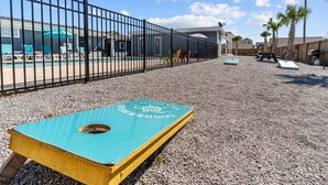A pool area with a blue and yellow shuffleboard table, a fenced pool, and a building with outdoor seating. - Loggerhead Inn & Suites - King Premium Suite in hotel in Surf City, North Carolina (Surf City)