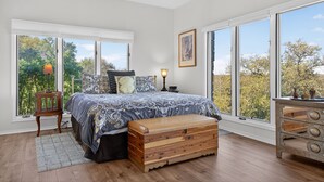 A bedroom with a large bed, a wooden chest, a dresser, and a window with a view of trees. - New! Luxury home with Views & Hot Tub, Game Room! (Horseshoe Bay)