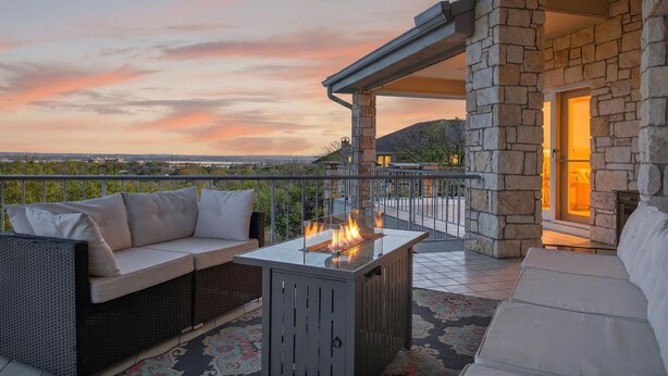 A covered outdoor seating area with a stone fireplace, a sofa, and a fire feature. - New! Luxury home with Views & Hot Tub, Game Room! (Horseshoe Bay)