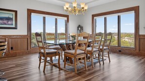 A dining area with a glass-top table, wooden chairs, a chandelier, and large windows with a view. - New! Luxury home with Views & Hot Tub, Game Room! (Horseshoe Bay)