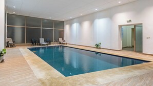 Een binnenzwembad met betegelde vloer, lounge stoelen en een glazen wand.