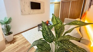 Een moderne woonkamer met een flatscreen televisie aan de muur, een bank, een salontafel en een potplant.