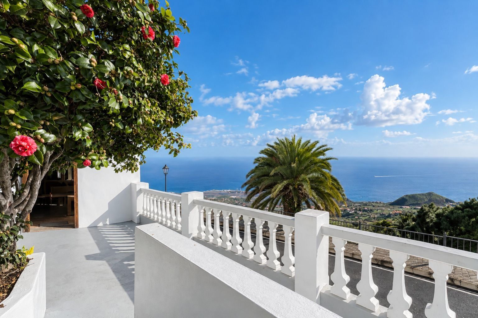Un balcón con barandilla blanca que da a un paisaje costero con cielo despejado y vista al mar.