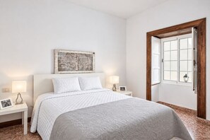 A bedroom with a bed, two bedside tables, a wall-mounted picture, and a window with a wooden frame. - GuestReady - Villa Private Pool (Santa Cruz de Tenerife)