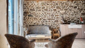 Una pared de piedra, un sofá, dos sillones estampados, una mesita y un mueble de madera.