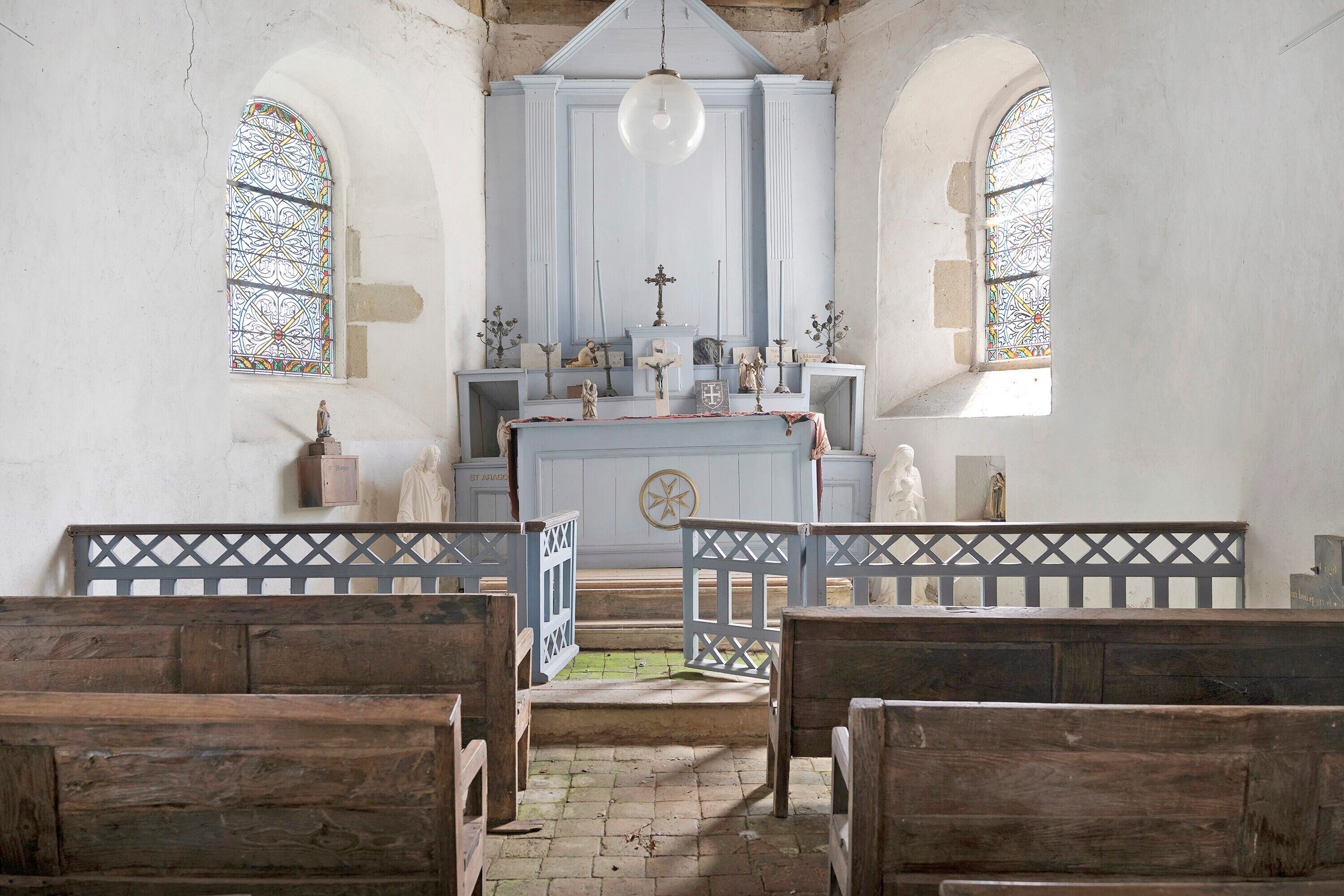 A church interior with wooden pews, a central altar, and stained glass windows.